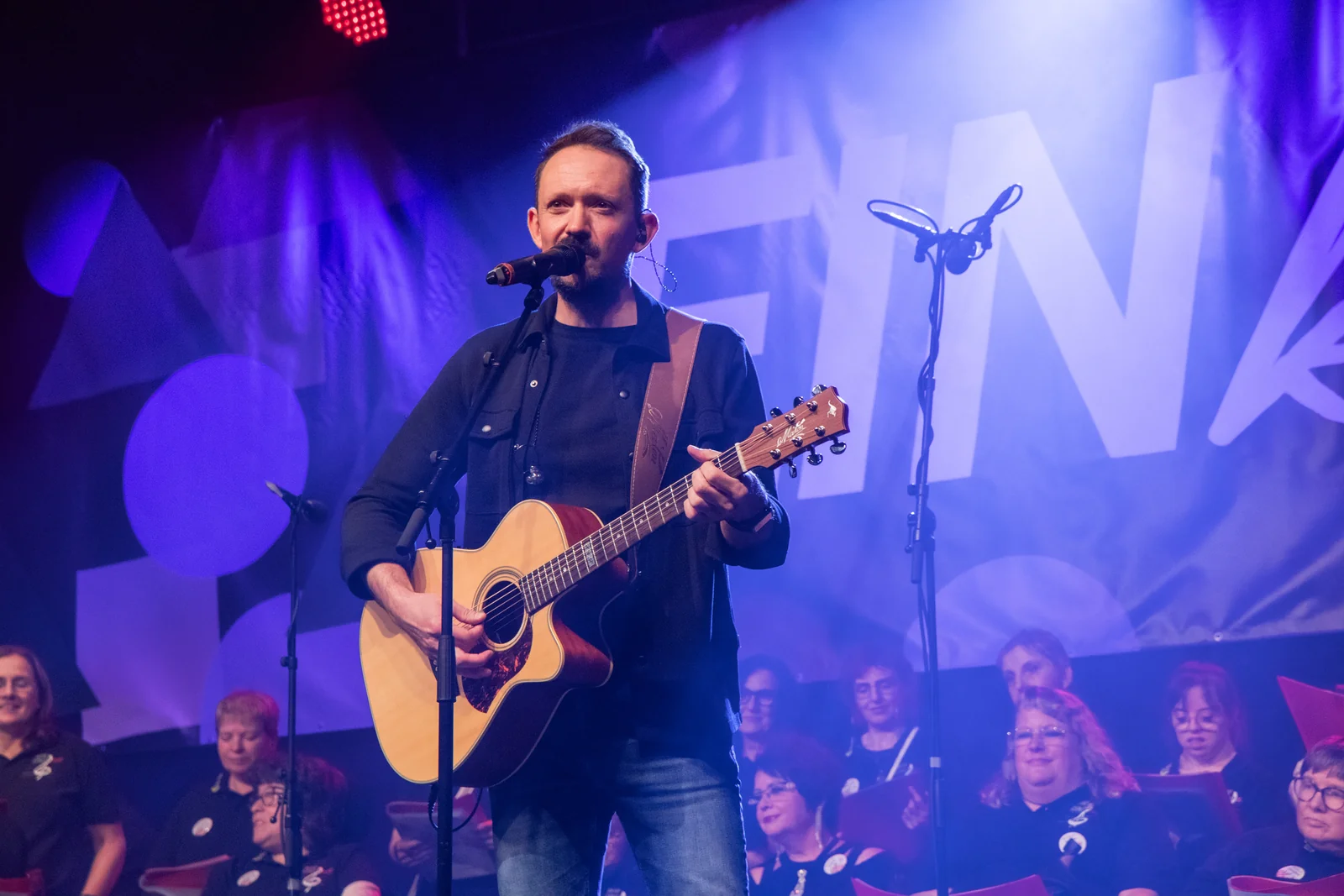 Kolja Koglin singt mit Akustikgitarre vor dem Chor bei EINklang 2026.